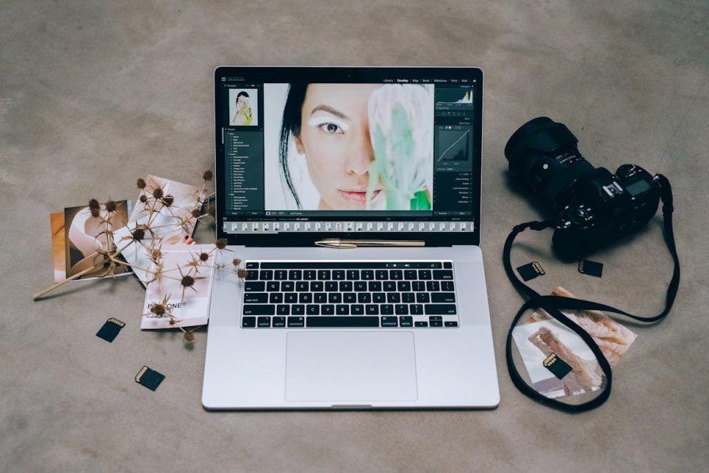 A stylish photography setup with a laptop editing a portrait and a camera surrounded by SD cards on a concrete surface.